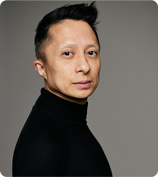 Professional portrait of Kwok One in a dark pinstripe suit against a grey background – corporate headshot with confident expression and formal attire.