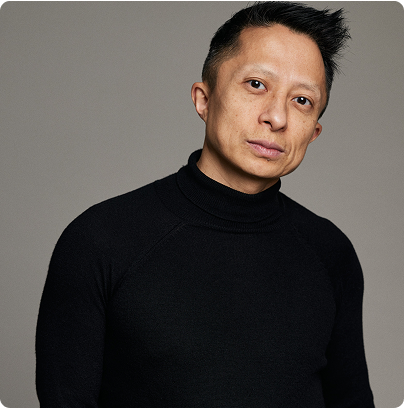 Professional portrait of Kwok One in a dark pinstripe suit against a grey background – corporate headshot with confident expression and formal attire.