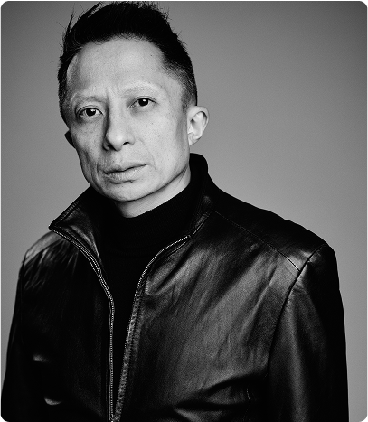 Professional portrait of Kwok One in a dark pinstripe suit against a grey background – corporate headshot with confident expression and formal attire.