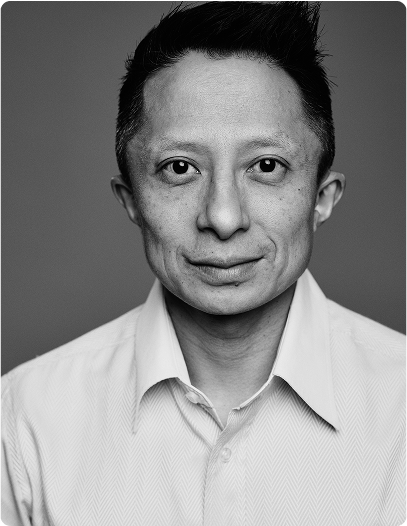 Professional portrait of Kwok One in a suit against a grey background – corporate headshot with confident expression and formal attire.